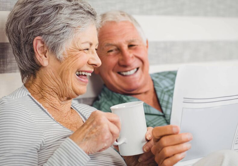 Elderly couple smiling and laughing while holding tea and medical paperwork, reflecting well-being with medical cannabis UK therapy